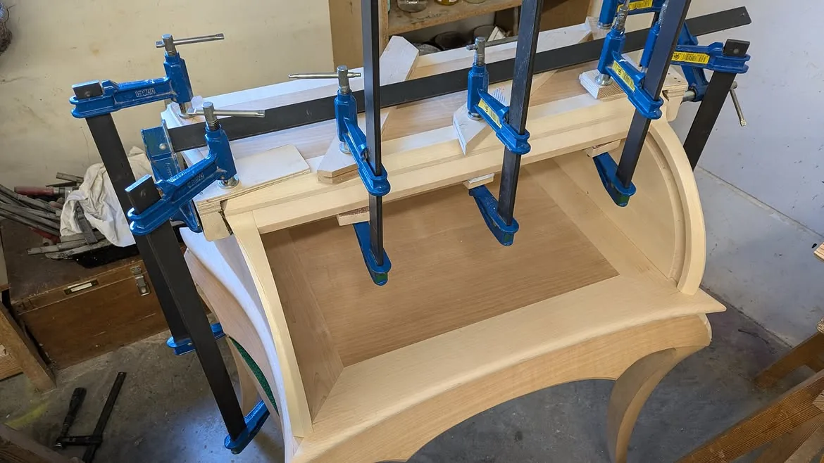 Corps supérieur courbe du bureau maintenu par plusieurs serre-joints pendant l’assemblage