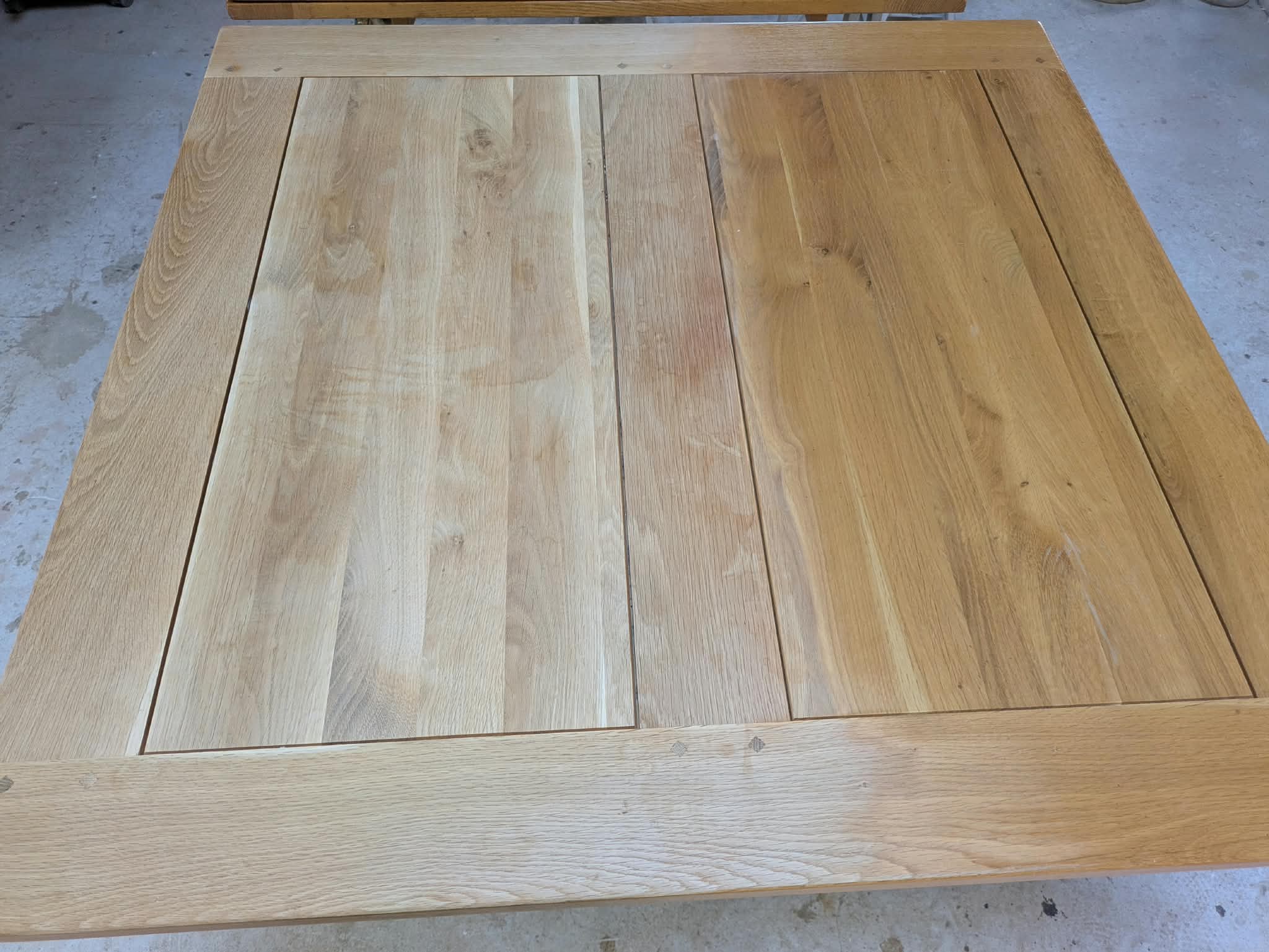 Plateau de la table en chêne à l’atelier, avec une partie poncée claire et une partie encore jaunie